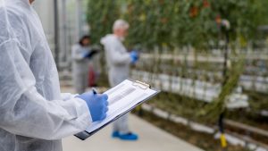 Male botanist writing notes on clipboard in greenhouse