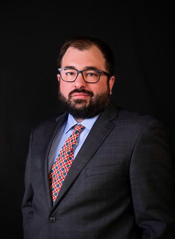 Dr. David Brew's Headshot, he wears glasses and a suit. He has dark hair and a beard.