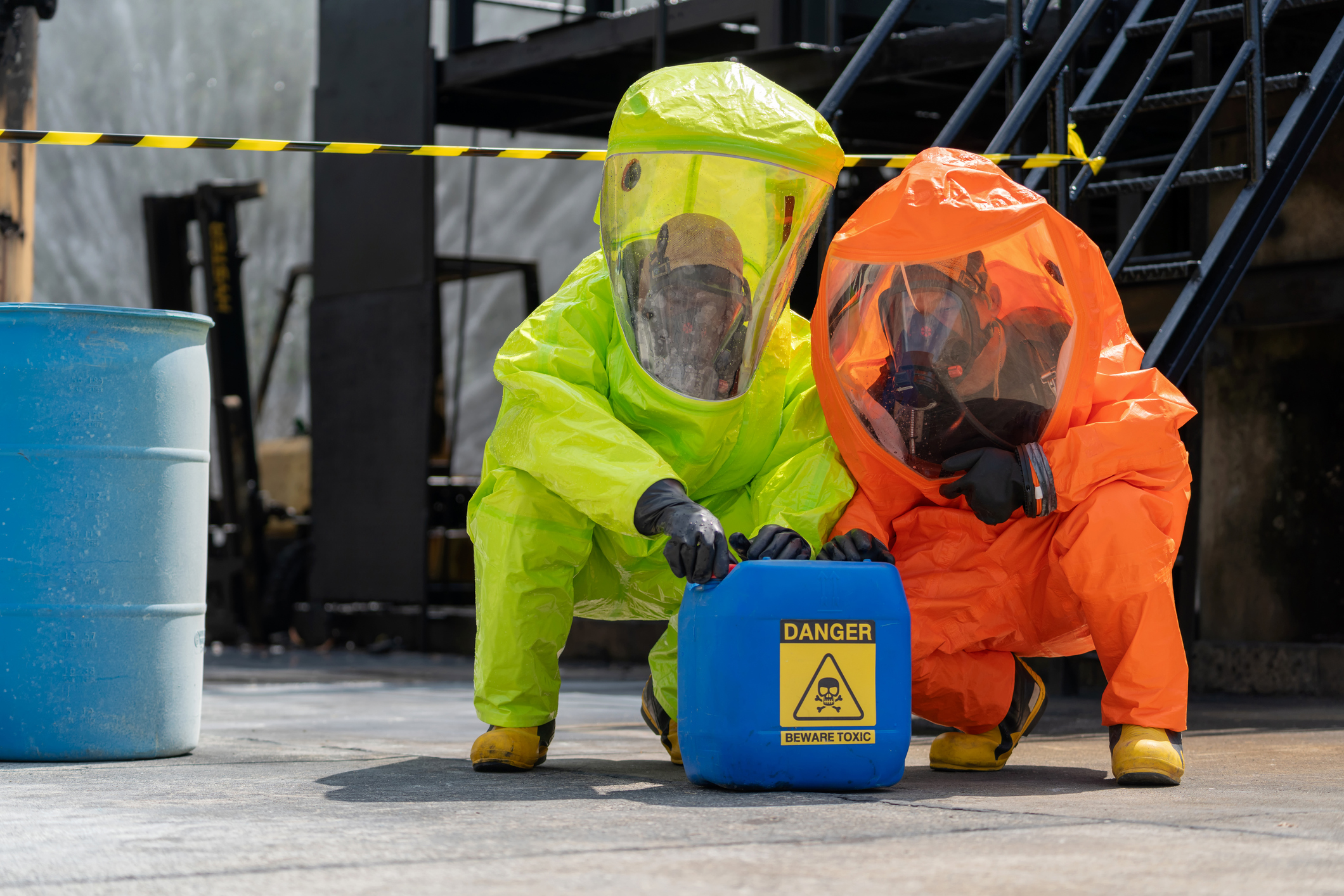 Two people wearing HAZMAT suits open a container that reads "danger beware Toxic"
